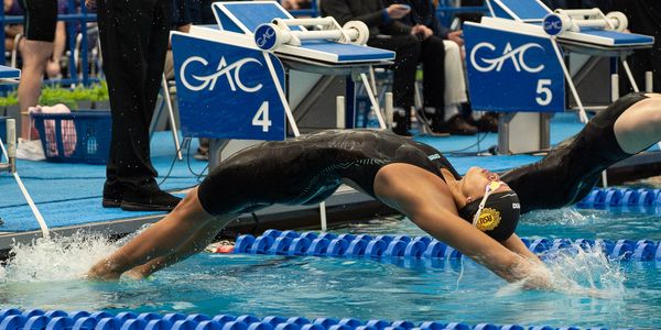 Swimmer in black suit diving backwards into pool at lane 4 in a competition.