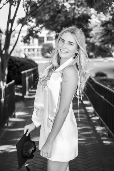 Young woman in graduation attire smiling outdoors on a sunny day.