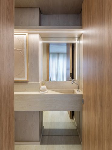 Lavabo revestido em madeira com bancada em travertino e pórtico iluminado com espelho