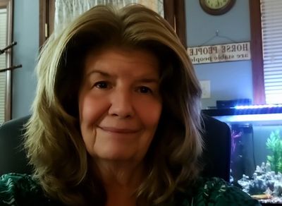 A smiling woman with voluminous hair sitting indoors.