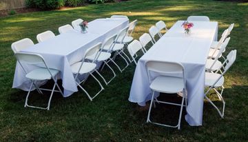 Two outdoor tables with white chairs and tablecloths.