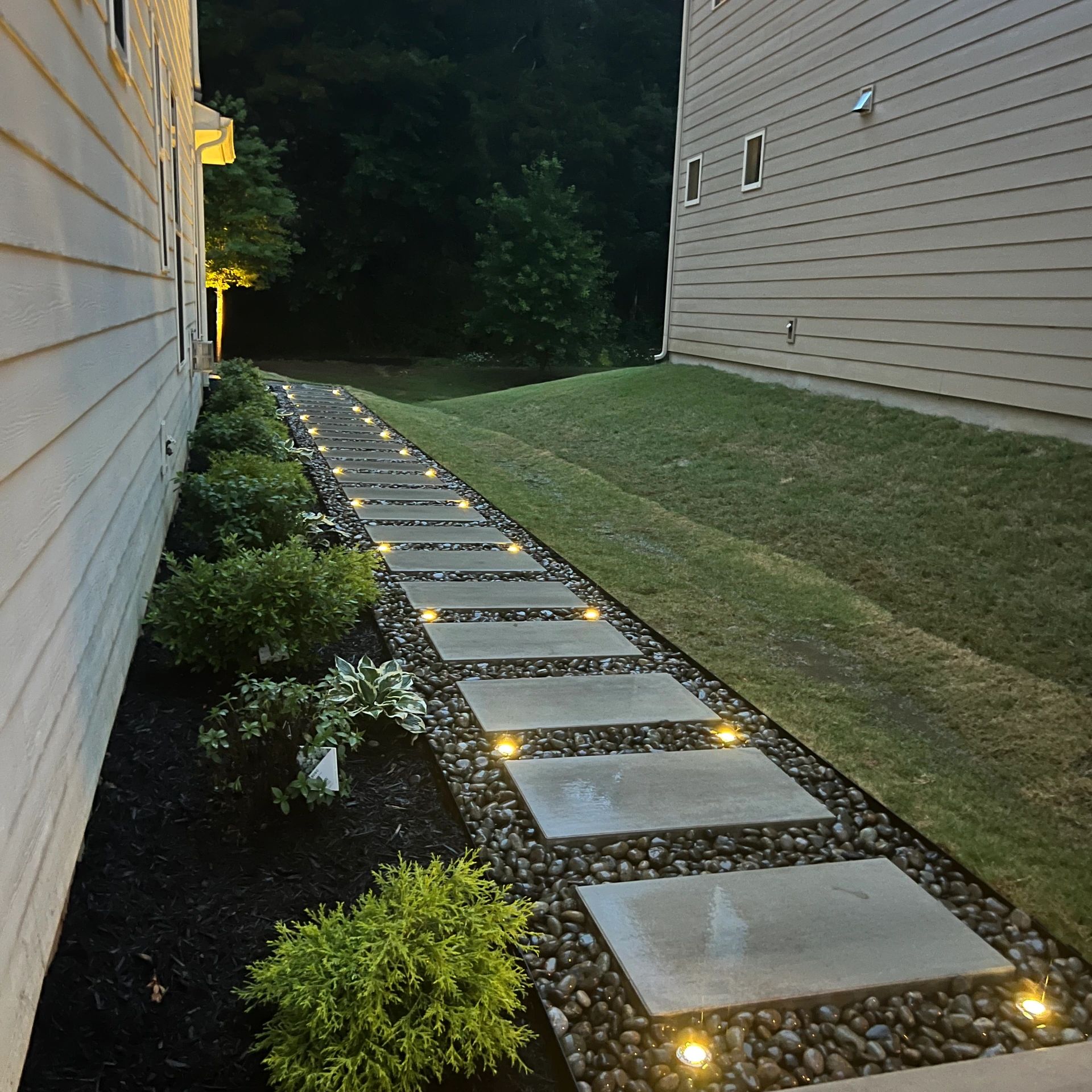 Illuminated stepping stone pathway between houses at dusk.