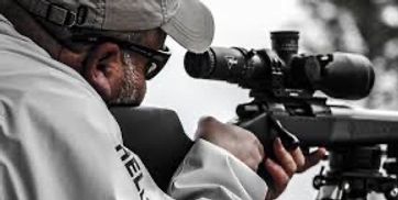 A man aiming through a sniper rifle scope with focus and precision.