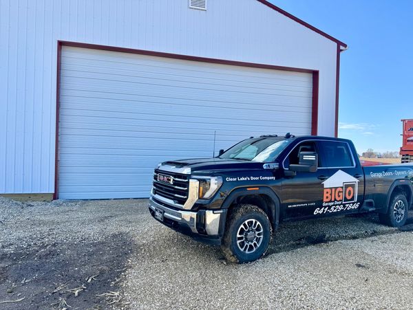 Black GMC truck parked outside a large garage door with company branding.