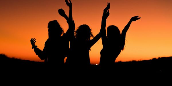 Silhouettes of three people joyfully raising their arms at sunset.