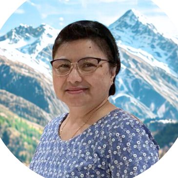 Smiling woman with glasses in front of snowy mountain scenery.