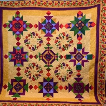 Colorful quilt with geometric and floral patterns bordered by a floral design.