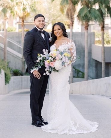 Groom in tux. Bride in wedding dress with hair and makeup, holding flower bouquet.