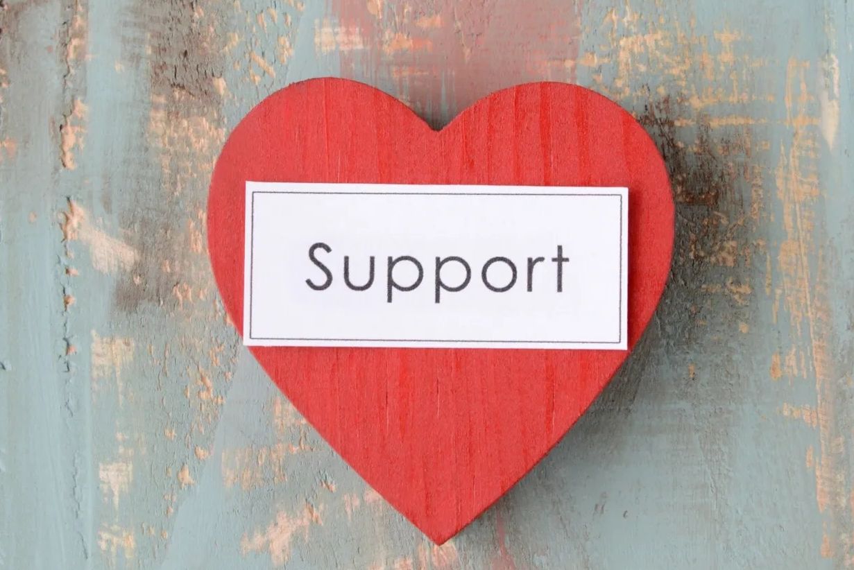Red heart with the word 'Support' on a textured wooden surface.