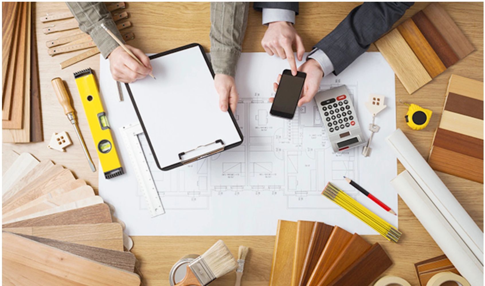 Two people reviewing architectural plans with tools and wood samples.