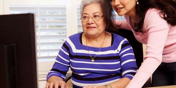 Senior woman using computer with help from younger woman.