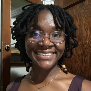Smiling woman with dreadlocks and glasses.
