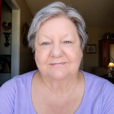 Smiling elderly woman with gray hair in purple top.