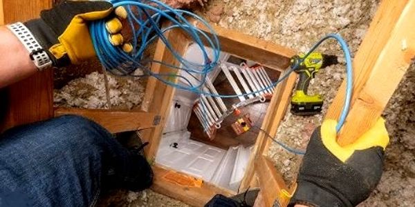 A worker pulling a cable through an attic with tools nearby.
