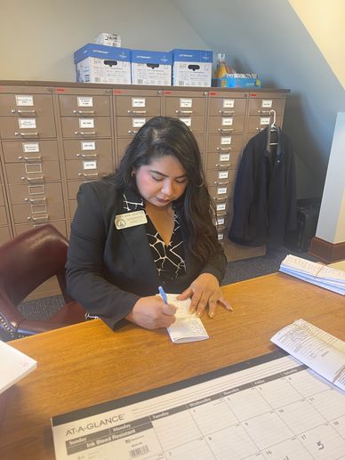 A woman in an office writing on a notepad at a desk.