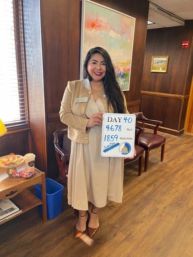 Woman in beige dress and jacket holding a board with numbers indoors.