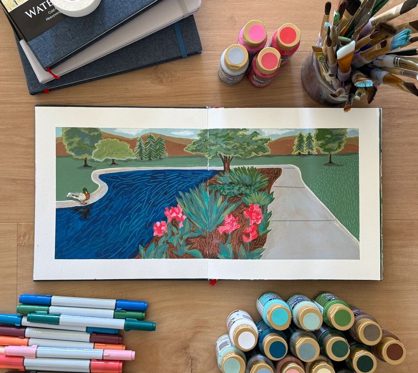 Open sketchbook with a landscape painting and art supplies around it.