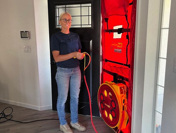 Woman operating a blower door test setup at a home entrance.
