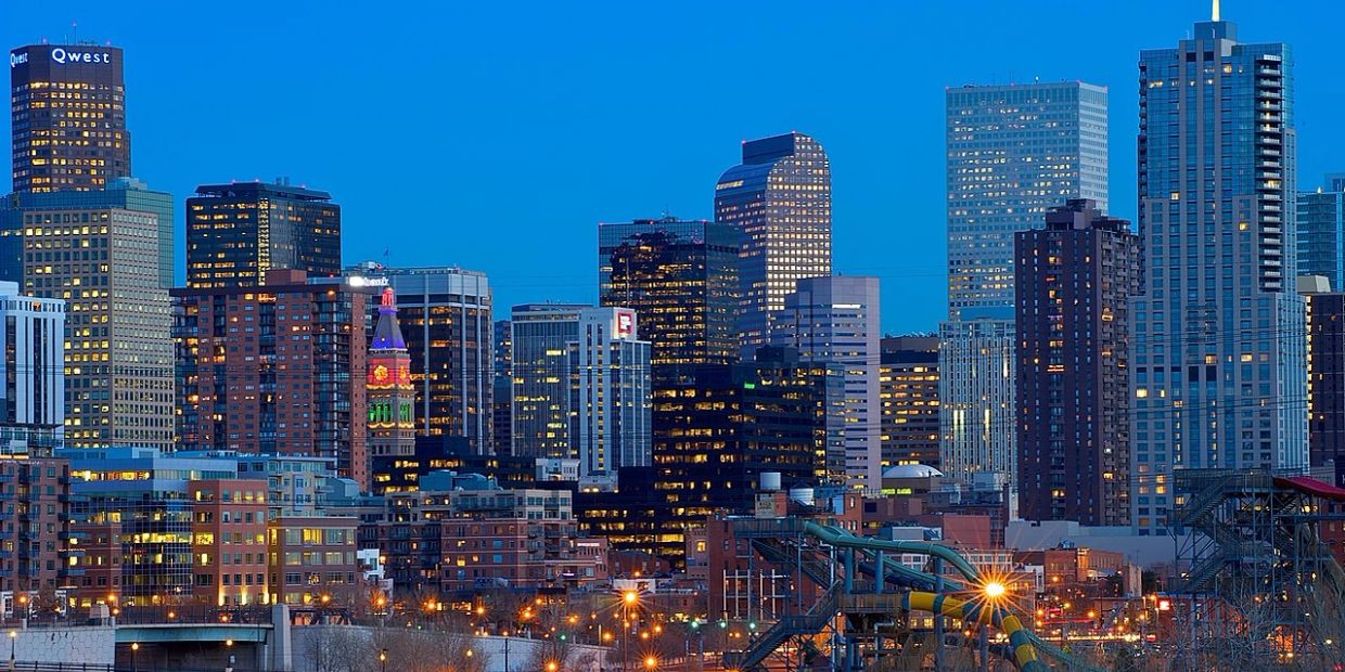 Evening cityscape of Denver with illuminated skyscrapers against a deep blue sky.