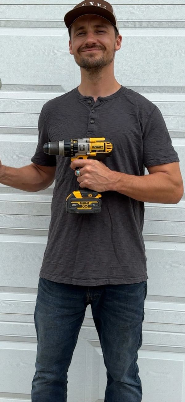 Man smiling and holding a yellow and black DeWalt power drill.