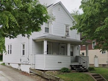 A white two-story house with a porch surrounded by trees.