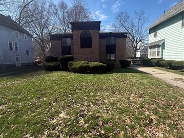 Brick house with trimmed bushes and a large front yard under a clear sky.
