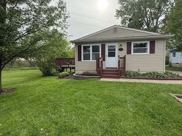 Small beige house with maroon shutters and a green lawn.