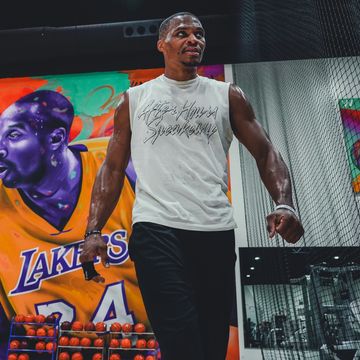 Man in gym attire walking confidently with a basketball mural in the background.