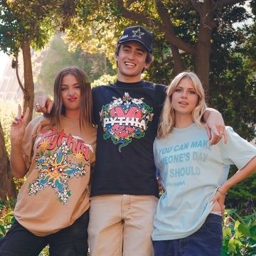 Three friends smiling outdoors, wearing colorful graphic t-shirts.