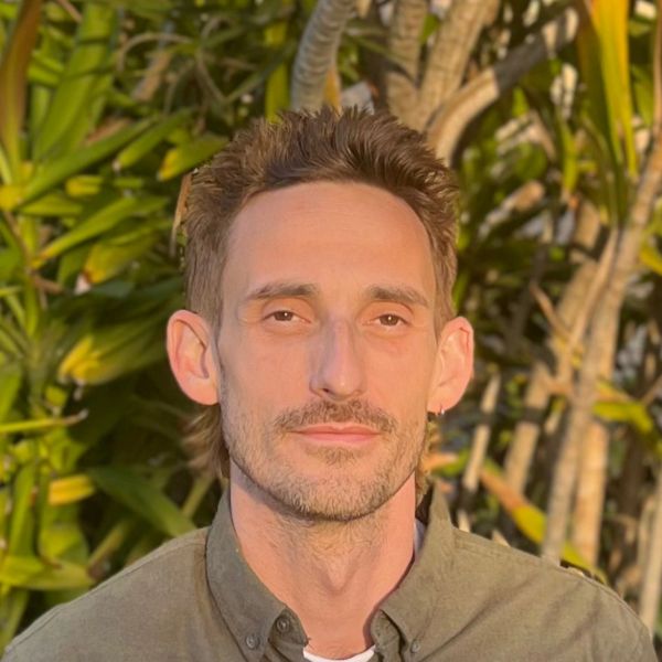 Man posing outdoors with leafy background.