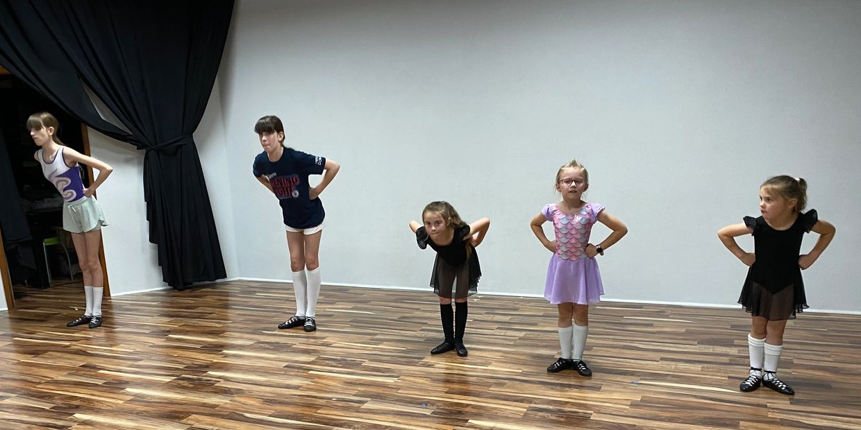 Five children in dance attire practicing a pose in a studio.