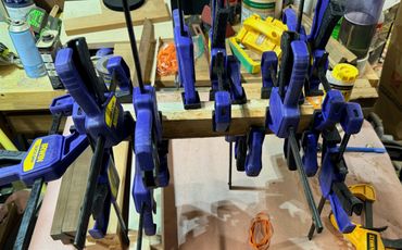 Multiple blue clamps holding pieces of wood together in a workshop.