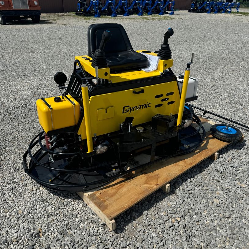 Yellow ride-on power trowel machine on gravel surface with dual joysticks.
