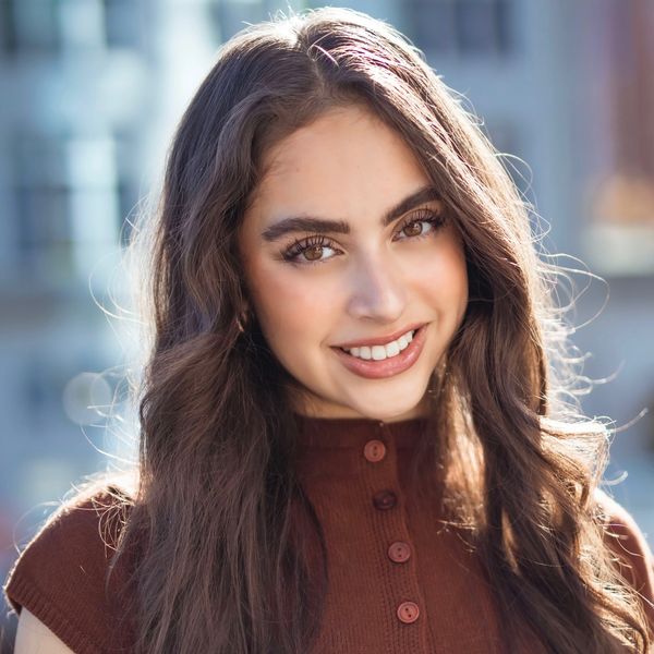 A young woman with long brown hair smiling warmly outdoors.