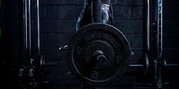 Person lifting a heavy barbell in a dark gym setting.