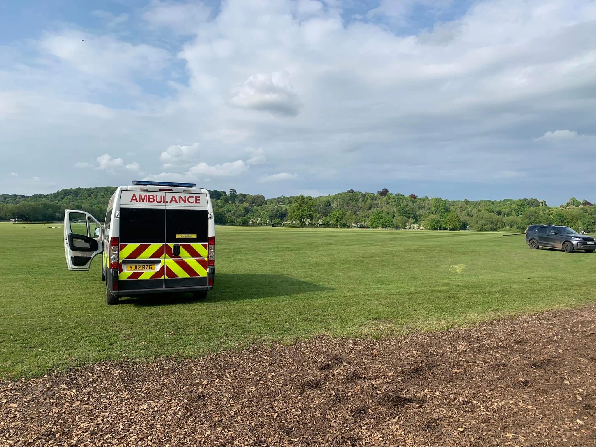 Ambulance with open door on a grassy field under a partly cloudy sky.