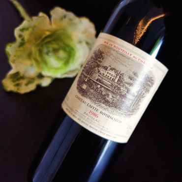 A vintage 1986 Château Lafite Rothschild wine bottle with a green flower in the background.