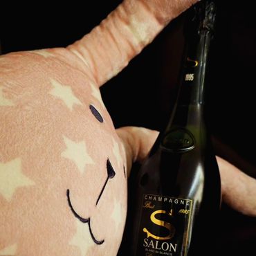 Plush toy holding a bottle of Salon champagne against a black background.