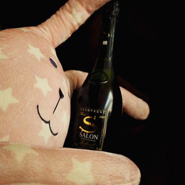 Plush toy holding a bottle of Salon champagne against a black background.