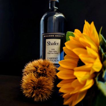 A wine bottle, sunflower, and autumn chestnut on a black background.