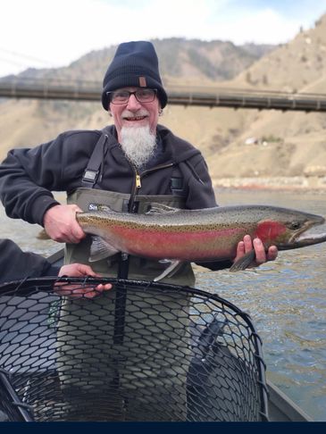 Man holding a large Steelhead while fishing on a river.