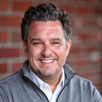 Smiling man in casual gray jacket against brick wall.