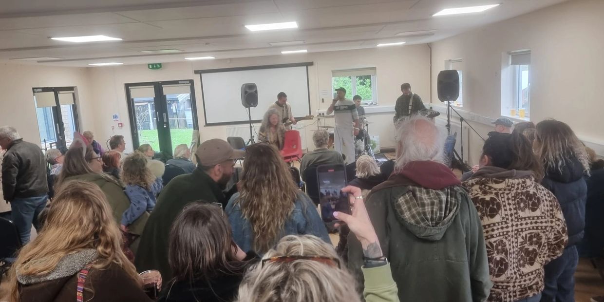 Crowd watching a live band perform indoors in a community hall.