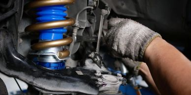 A person working on a car suspension with a coil spring and shock absorber.