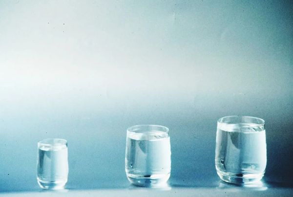 Three clear glasses filled with different amounts of water against a soft blue background.