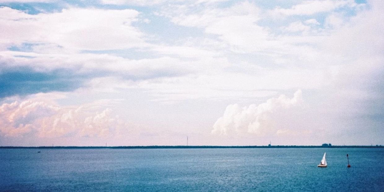 A small sailboat on a vast blue sea under a cloudy sky.