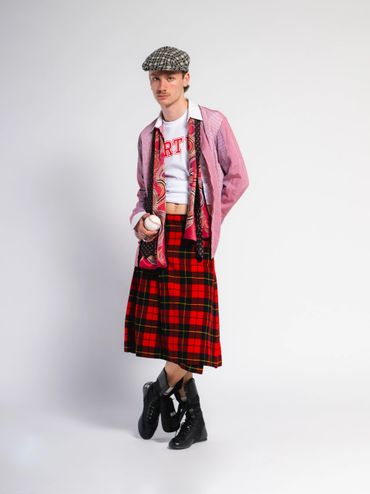Fashion-forward individual in a red plaid skirt, crop top, and patterned cap.