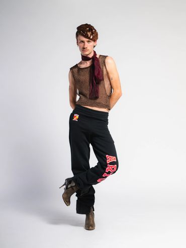 Fashion-forward individual poses in eclectic outfit with sequined headpiece and graphic sweatpants.