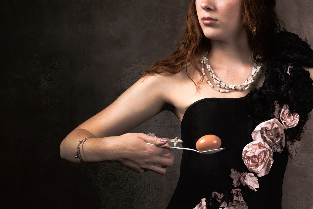Woman in black dress holding an egg on a spoon.