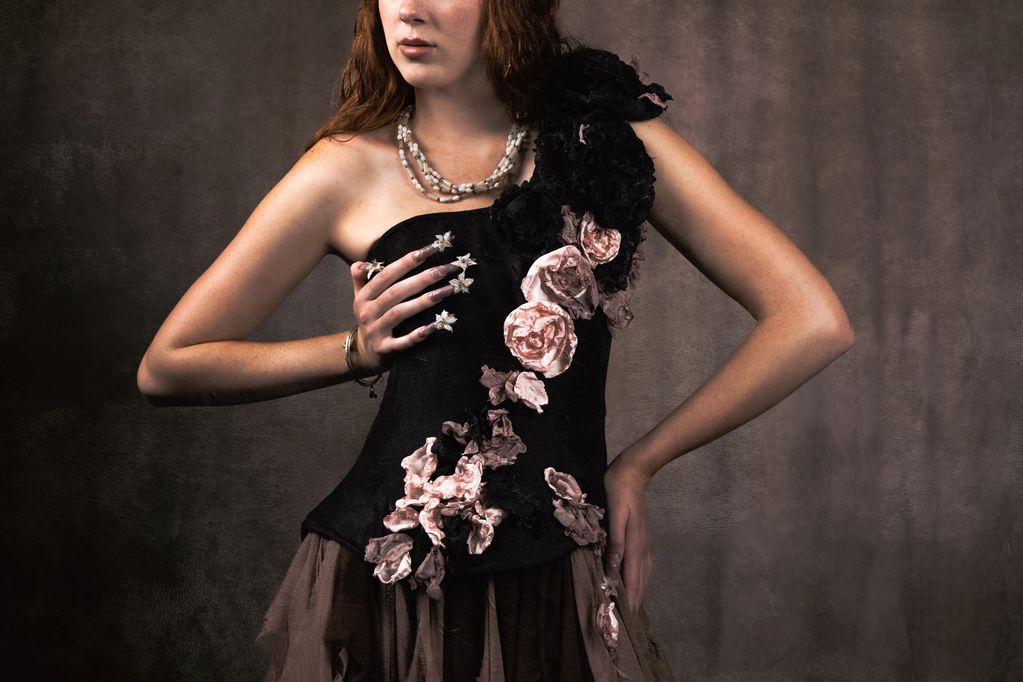 Woman in floral dress poses with hand on chest and waist.